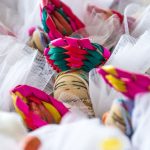 bomboniere cresima con confetti in sacchetti di tulle colorati e decorati con bamboline abbellite con cesti in testa vivaci e differenziati provenienti dal Guatemala con calamita sul retro.